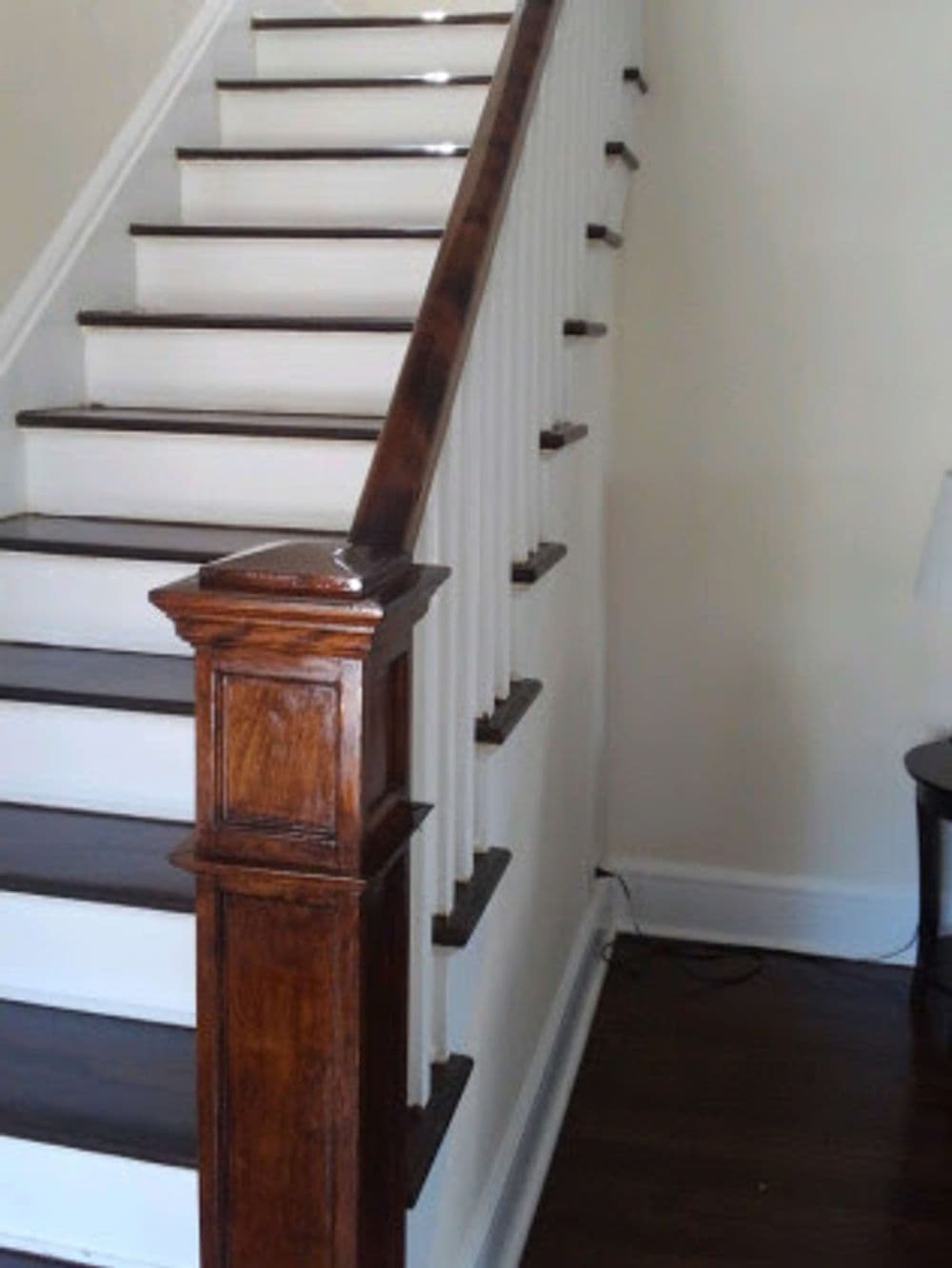 Wooden staircase with white railings and dark brown steps, featuring a detailed post design.