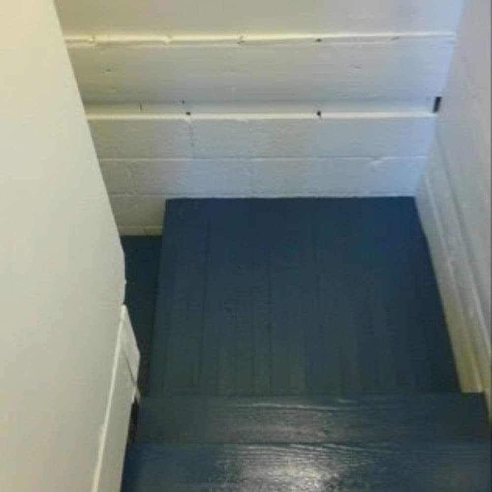 Blue wooden stairs leading down a hallway with white walls.