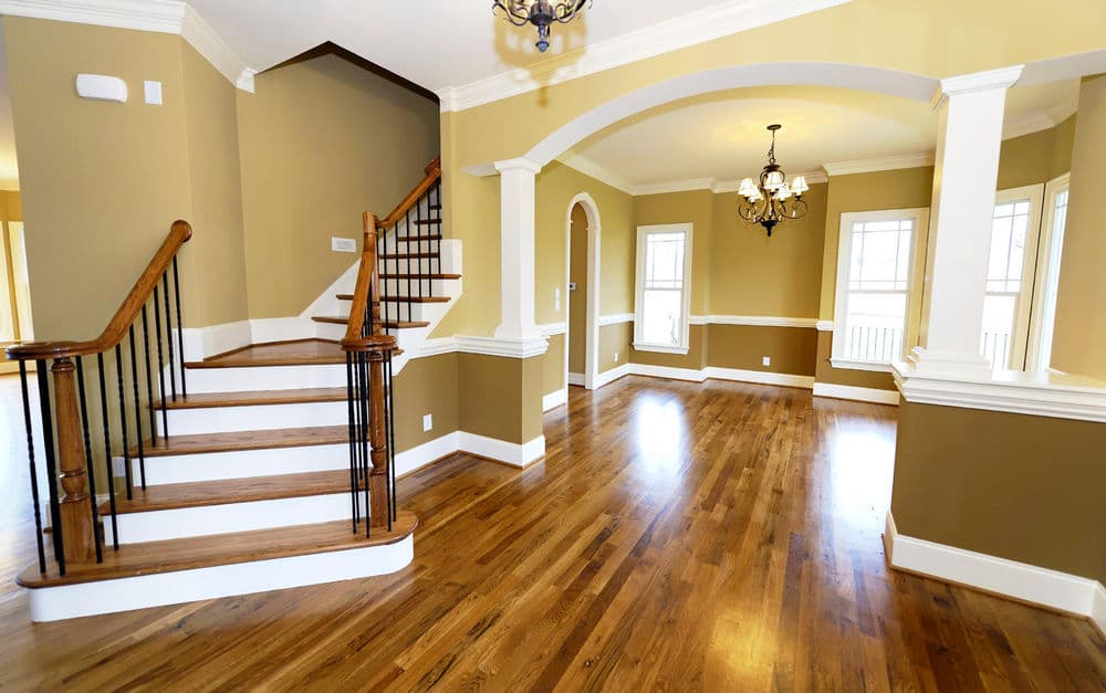 Spacious living area with hardwood floors, staircase, and decorative archway.