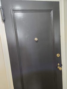 Closed black door with a peephole and three brass locks and knobs, framed by a white door frame.