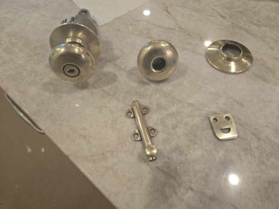 Disassembled brass door knob set with knobs, rosette, latch bolt, and strike plate on a marble surface.