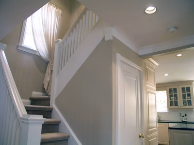 Staircase with carpeted steps and white railing next to a kitchen area with light cabinets and a closed door.