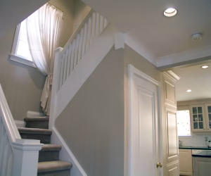 Staircase with carpeted steps and white railing next to a kitchen area with light cabinets and a closed door.