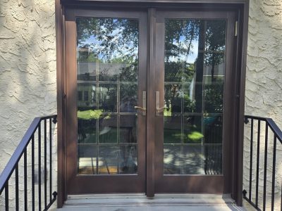 Brown double doors with glass panes open onto a small outdoor landing with black metal railings.