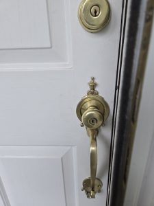 Close-up of a white door with a brass handle, deadbolt, and door frame partially visible on the right side.